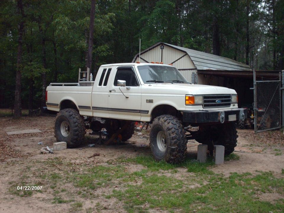 White lifted pickup truck with large tires parked in a yard with a shed in the background