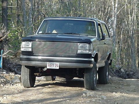 1993 Ford Bronco - Front view of a 1993 Ford Bronco parked on a dirt road with trees in the background.