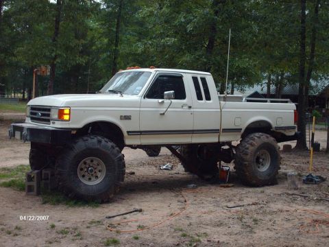 1990 Ford F-150 - White 1990 Ford F-150 pickup truck modified with a significant suspension lift and oversized tires.