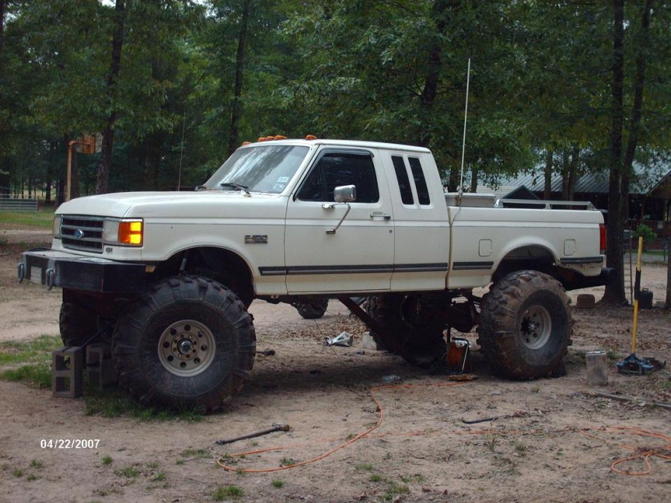 1990 Ford F-150 pickup truck with large off-road tires and suspension lift, parked outdoors