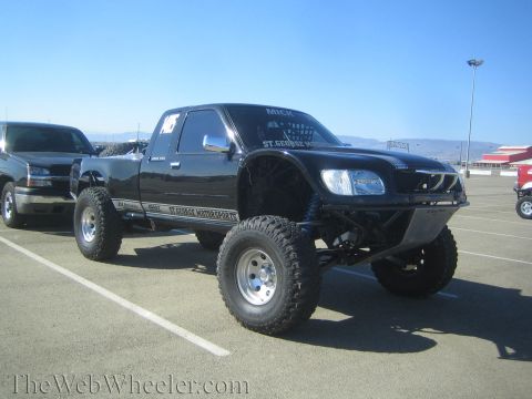 1990 Ford Bronco - black lifted prerunner pickup truck on large tires with aftermarket fiberglass fenders parked in a lot beside other vehicles.