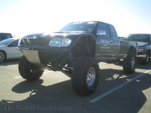 1990 Ford Bronco - black lifted prerunner pickup on tall suspension and large tires with a For Sale sign in the windshield, parked in a lot.