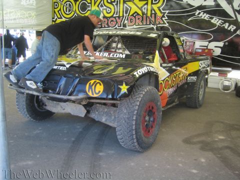 1990 Ford Bronco - man in jeans leans over the hood of a black Rockstar Energy Drink off-road race truck with KC and Toyo Tires graphics inside a pit tent.