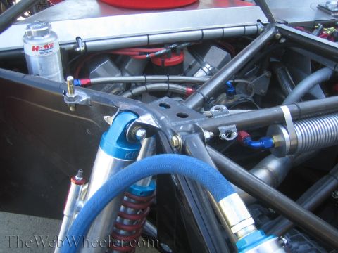 1990 Ford Bronco - Detailed close-up of a tube-frame chassis showing blue coilover shocks, braided fuel lines, a Howe canister and welded steel tubing.