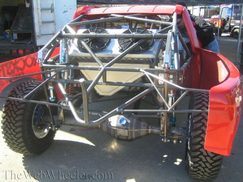 1990 Ford Bronco - Rear three-quarter view of a red off-road buggy showing its bare tube frame, dual radiator fans and blue coilover shocks.