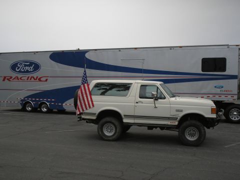 1990 Ford Bronco - A white 1990 Ford Bronco is parked beside a Ford Racing trailer, displaying an American flag.