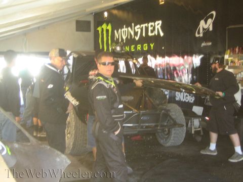 1990 Ford Bronco - young man in a Monster team jacket and sunglasses stands in front of an off-road truck under a black Monster Energy pit canopy.