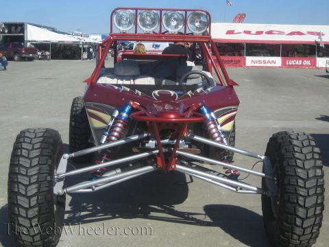 1990 Ford Bronco - Front view of a maroon open-cockpit off-road buggy showing exposed A-arms, blue coilover shocks and a four-light roof bar.