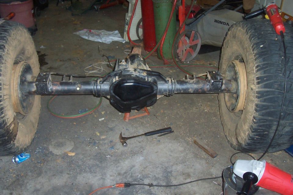 Rear axle assembly with two large tires mounted, resting on a workshop floor
