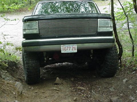 1993 Ford Bronco - This lifted Ford truck is shown from the front, navigating an off-road path with large tires.