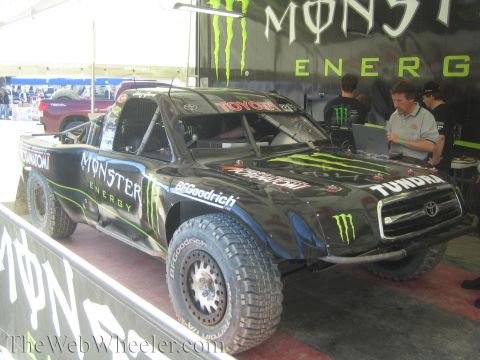 1990 Ford Bronco - black Monster Energy Toyota Tundra off-road race truck on display in a pit area as crew work at a laptop nearby.