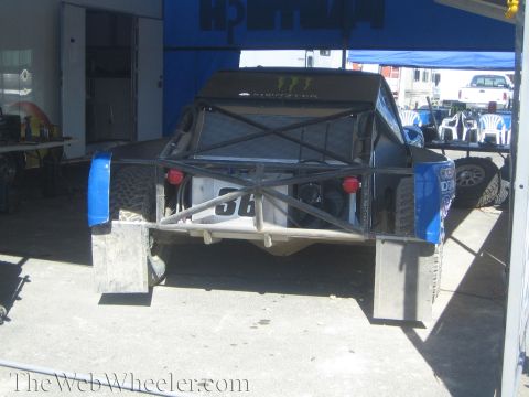 1990 Ford Bronco - Rear view of a number 56 off-road race truck with blue fenders and exposed tube frame parked under a pit canopy.
