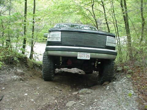 1993 Ford Bronco - A lifted black Ford Bronco navigates a rocky, wooded trail from a low front-angle perspective.