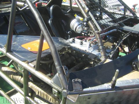 1990 Ford Bronco - open engine bay of a tube-chassis off-road racer shows the motor, a turbo, wiring and a black racing seat behind it.