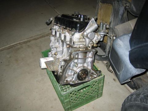 1987 Suzuki Samurai - Engine removed from a vehicle, resting in a green plastic crate on a concrete floor.