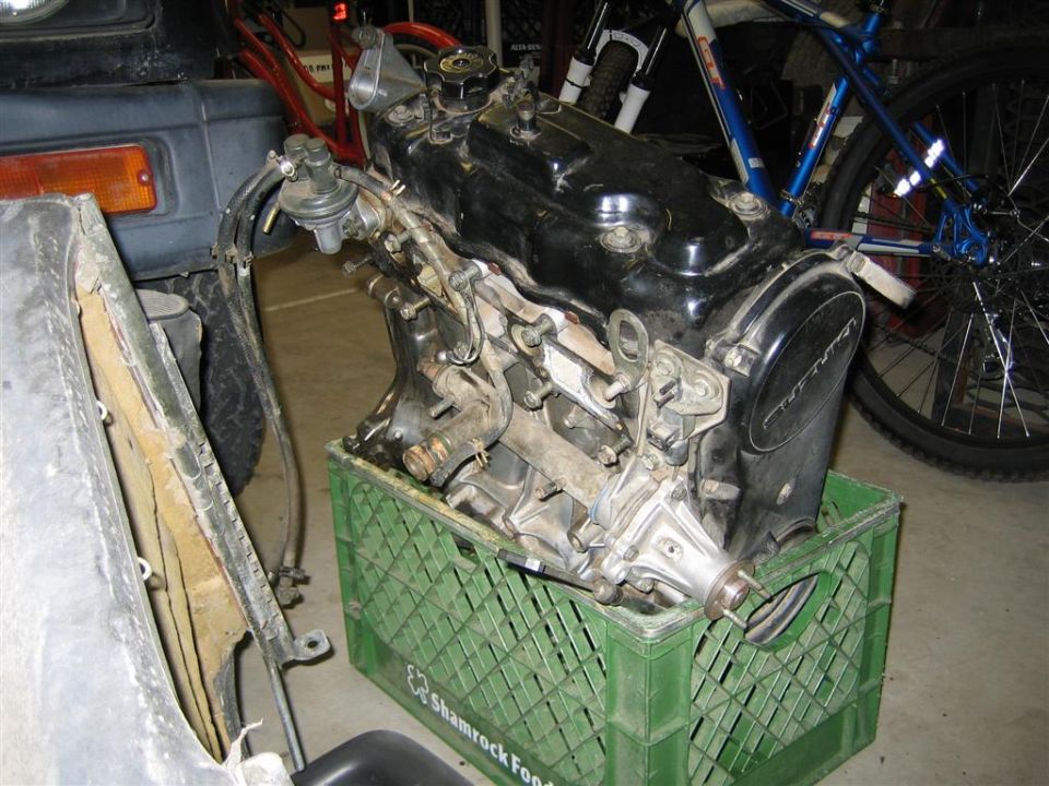 engine sitting on a green milk crate, with a bicycle in the background and part of a vehicle to the left
