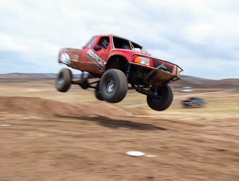 1992 Ford Explorer - A red off-road truck soars through the air during a jump, with another vehicle visible in the distance.