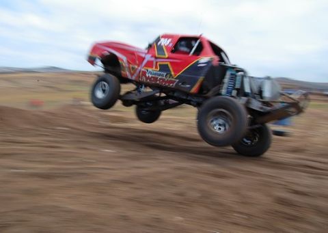 1992 Ford Explorer - A modified truck with large tires jumps over a dirt track during a race.