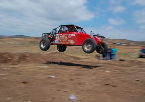 1992 Ford Explorer - Off-road buggy airborne over a dirt track, with spectators in the background.