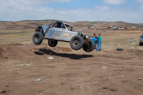 1992 Ford Explorer - This off-road buggy is captured mid-jump against a dusty, hilly landscape under a partly cloudy sky.