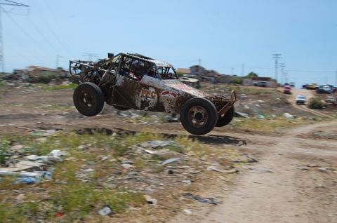 1992 Ford Explorer - An off-road buggy jumps over debris in a dusty, rural area with other vehicles in the background.
