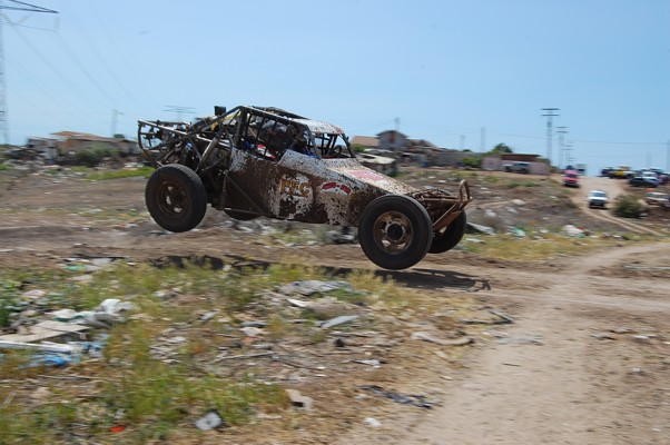 Mud-splattered off-road buggy mid-air, showing exposed roll cage and rusty body panels