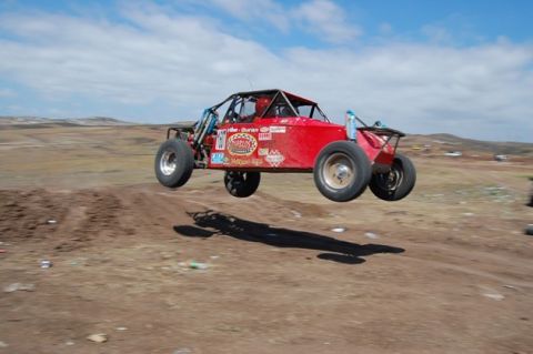 1992 Ford Explorer - This red dune buggy is airborne over a dirt track, captured mid-jump against a cloudy sky.