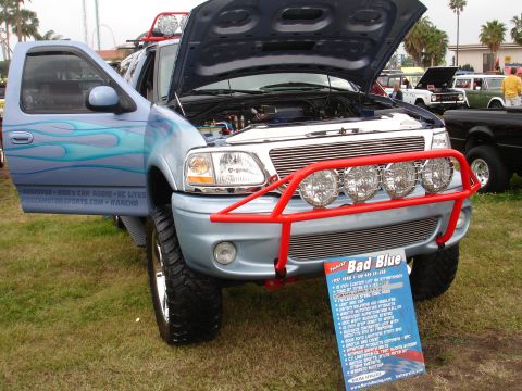 1993 Ford Taurus - This modified pickup truck, identified as 'Bad Blue', is displayed with its hood open and a descriptive sign.