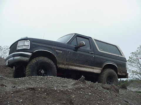 1993 Ford Bronco - A muddy black Ford Bronco is shown from the front 3/4 angle on a dirt terrain.