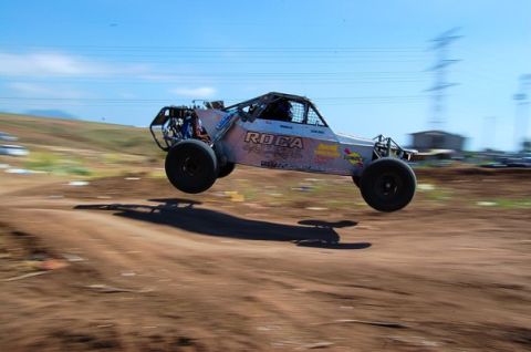 1992 Ford Explorer - A custom off-road buggy soars through the air over a dirt track.