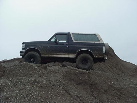 1993 Ford Bronco - A black 1993 Ford Bronco is seen from the side, parked on a dirt mound under an overcast sky.