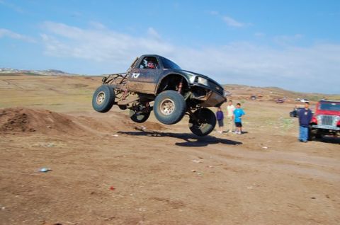 1992 Ford Explorer - A modified truck soars through the air during an off-road event, with spectators watching.