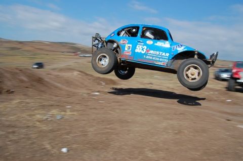 1992 Ford Explorer - A blue off-road buggy soars through the air during a race, with other vehicles visible in the background.