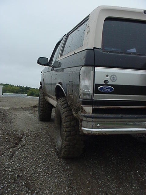 1993 Ford Bronco - The rear of a dark colored Ford Bronco with a tan removable top is shown from a low angle.