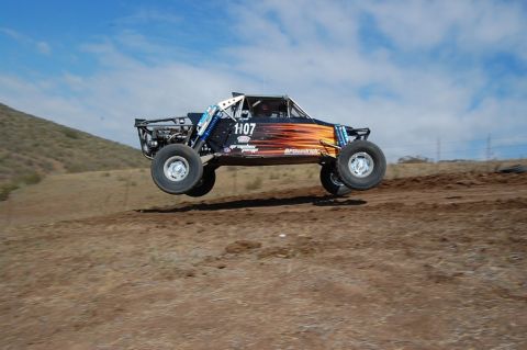 1992 Ford Explorer - A custom off-road buggy with number 1107 takes flight over a dirt track under a blue sky.