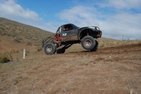 1992 Ford Explorer - A modified truck is airborne during an off-road race, kicking up dirt.