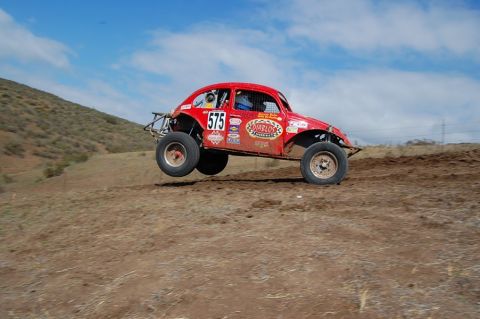 1992 Ford Explorer - A red off-road buggy jumps over a dirt track under a blue sky with scattered clouds.