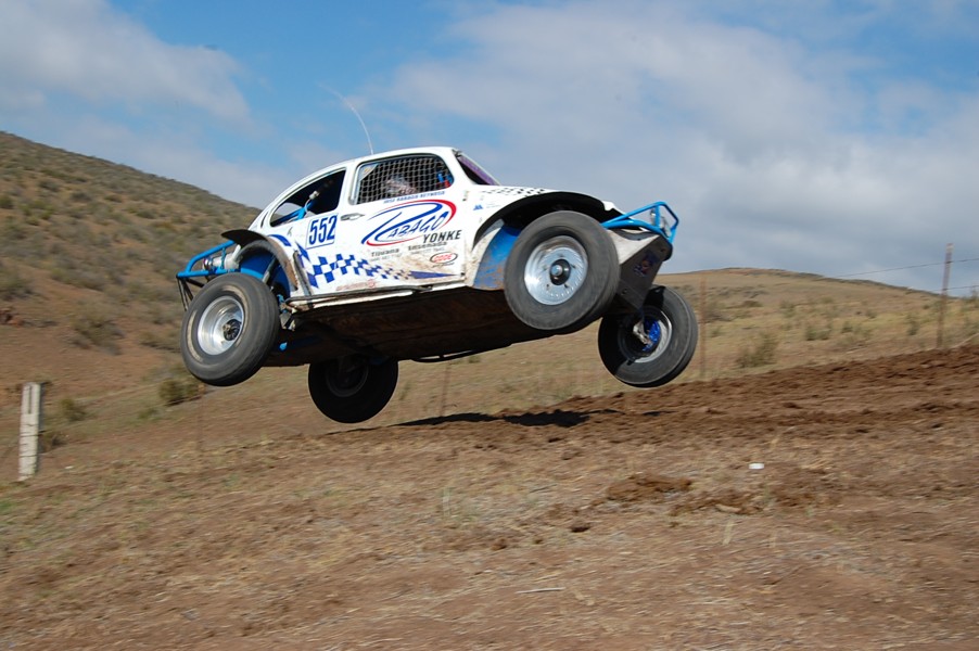 White off-road buggy with blue accents airborne over dirt track