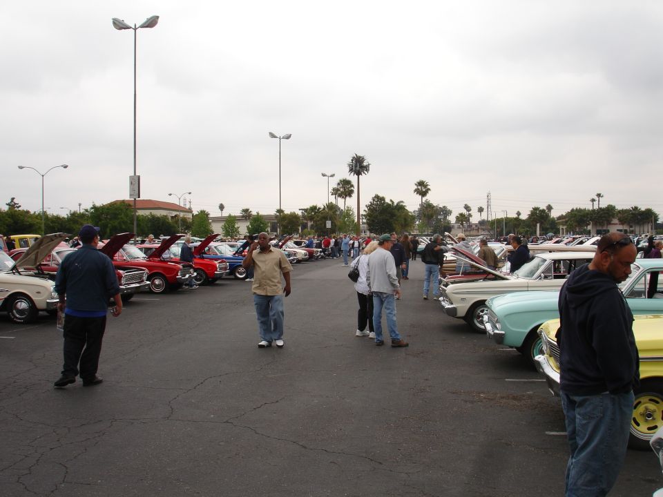 Outdoor car show with many classic cars parked in rows and people milling around
