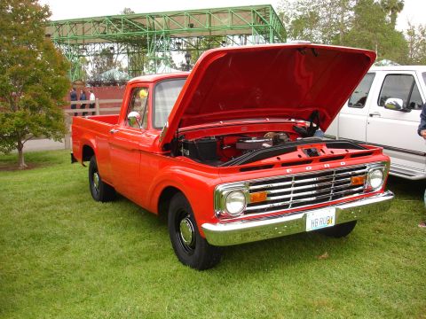 1993 Ford Taurus - A classic red Ford pickup truck is parked on a grassy lawn with its hood open, revealing the engine bay.