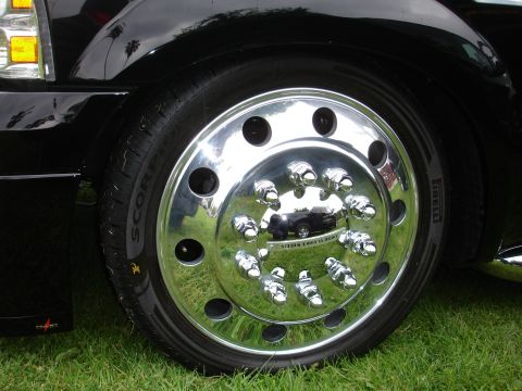 1993 Ford Taurus - A close-up view of a shiny chrome wheel with numerous lug nut covers, reflecting another vehicle in its surface.