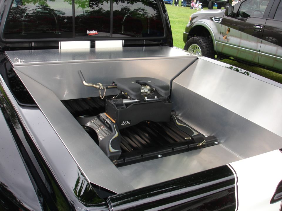 Truck bed with a fifth wheel hitch installed. Another truck is parked nearby