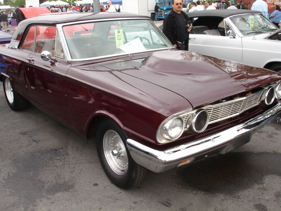 Maroon 1963 Ford Falcon Sprint coupe with scoop hood parked next to a white convertible