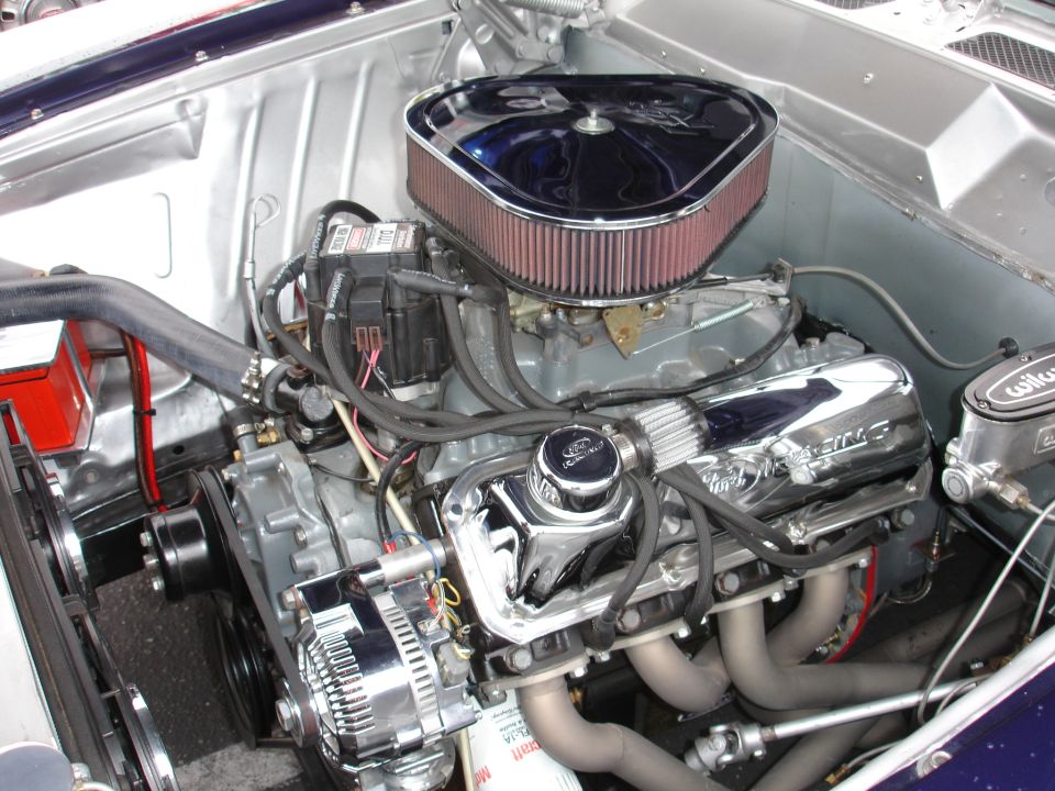 Close-up of a Ford V8 engine, showing chrome valve covers, air cleaner, alternator, and exhaust headers