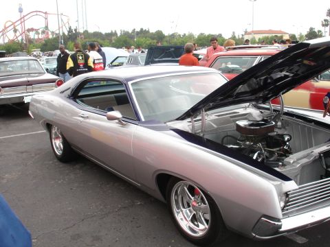 1993 Ford Taurus - A silver coupe with its hood open, revealing the engine, sits in a parking lot with other vehicles and people around.