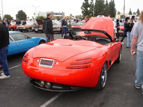 1993 Ford Taurus - A red convertible concept car is displayed at an outdoor car show, with other vehicles and people around.