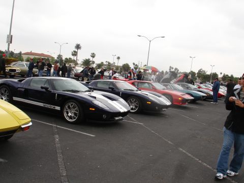 1993 Ford Taurus - A line of Ford GT sports cars are parked in a lot, with people milling around them.