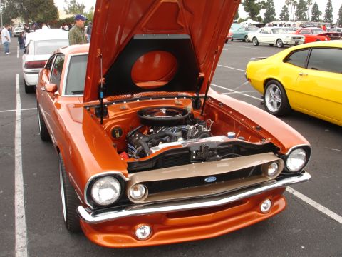 1993 Ford Taurus - An orange classic car is parked with its hood open, revealing the engine bay and a Ford emblem on the grille.