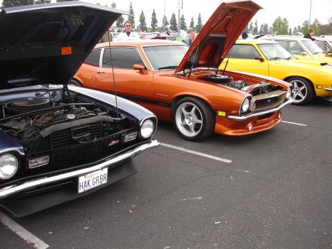 1993 Ford Taurus - Two classic coupes, one orange and one blue, are parked side-by-side with their hoods open at an outdoor car show.