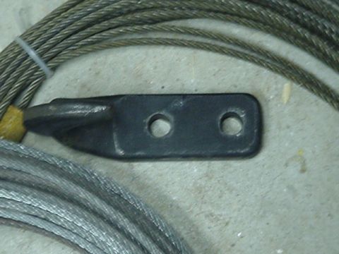1993 Ford Bronco - Close-up of a coiled steel winch cable laid on a concrete floor, with the swaged end fitting attached to a flat black steel bracket drilled…